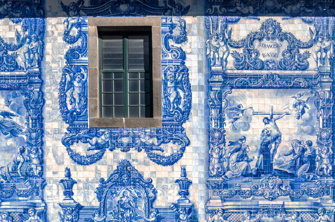 Fachada coberta por azulejos azuis e brancos, com cenas religiosas, anjos, molduras decoradas e uma janela central.
