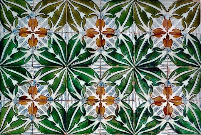 Painel de azulejos com folhas verdes, frutos amarelos e detalhes em relevo sobre fundo claro.
