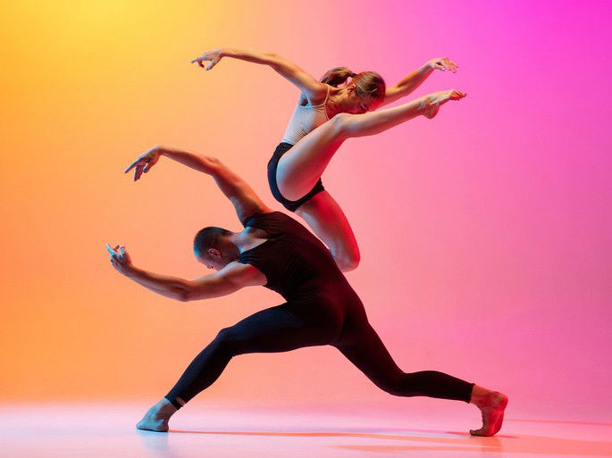 Casal dançando dança contemporânea em um fundo gradiente amarelo-rosa colorido sob luz neon.