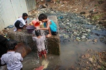 Crianças no meio do lixo utilizando água suja