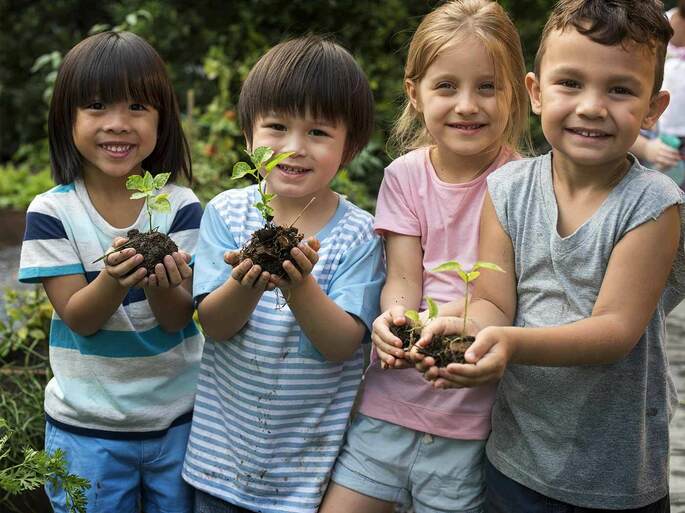 crianças felizes segurando plantinha com terra nas mãos