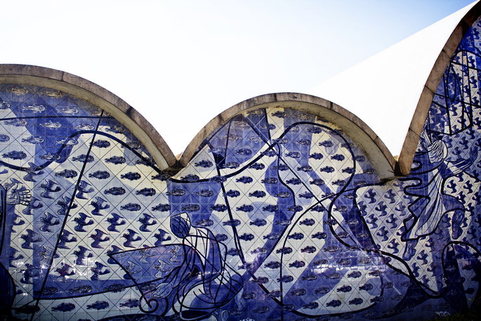 Vista lateral de uma igreja de formas curvas, revestida por um painel azul e branco, ao lado de uma &aacute;rea com &aacute;gua.