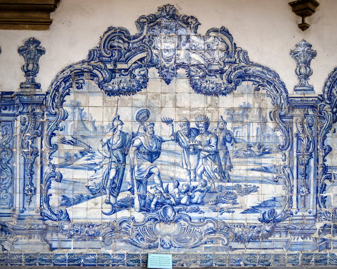 Painel de azulejos azuis e brancos com uma cena formada por pessoas, &aacute;rvores e elementos decorativos.