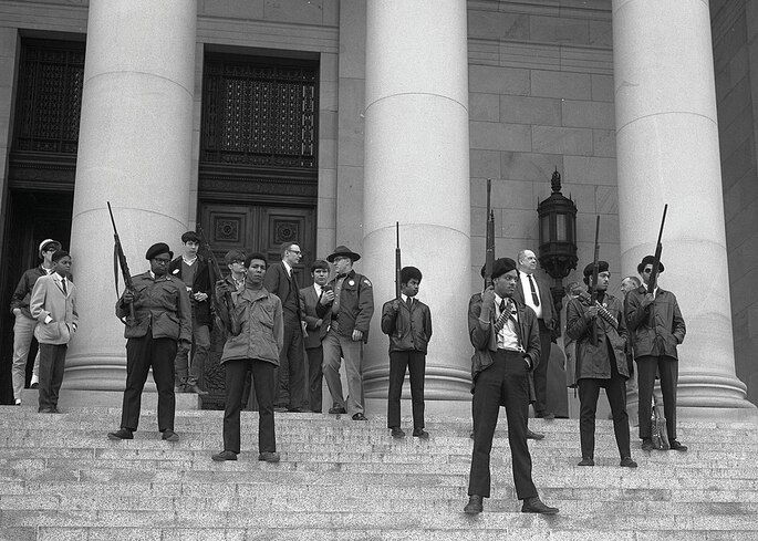 Membros armados dos Panteras Negras em uma manifestação frente a um prédio.