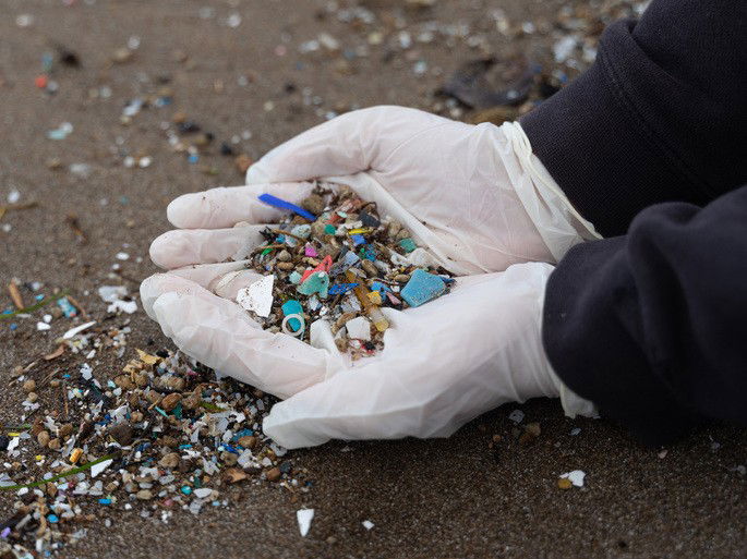 Mãos mostrando microplásticos na praia