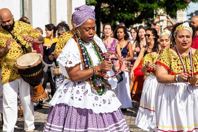 Samba de roda da nega Duda mostra mulheres com  saias rodadas e mulher negra cantando.