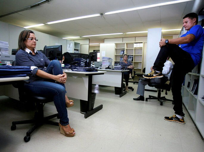 Trabalhadores fazendo ginástica laboral dentro do escritório com a supervisão de um professional