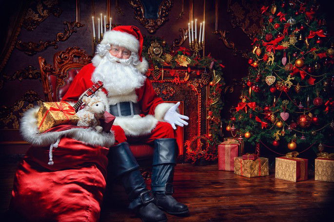 Papai Noel sentado junto à árvore de Natal e à lareira