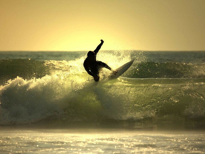 Surfista fazendo a manobra da batida, onde ele bate a borda da prancha na crista da onda